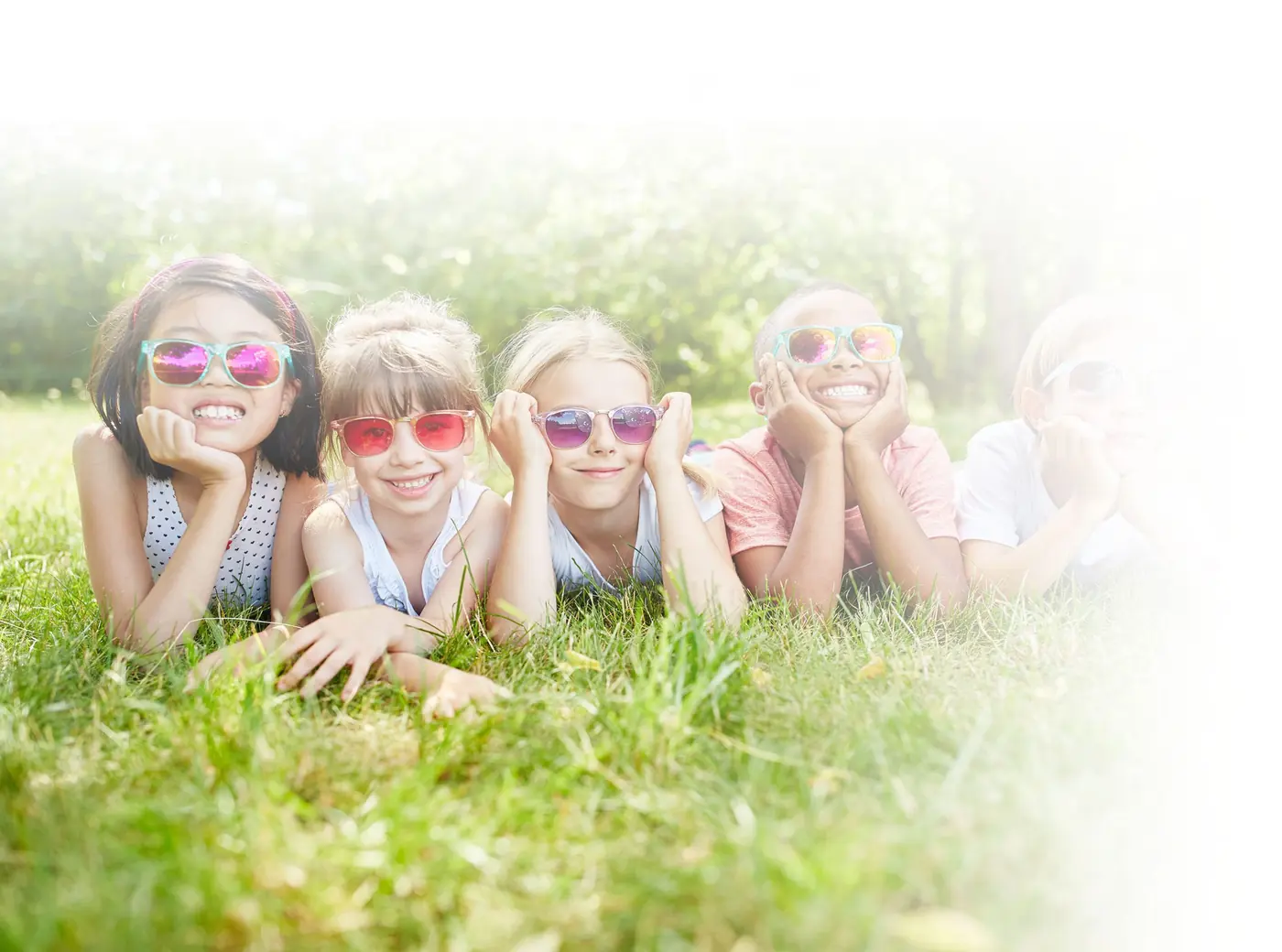 Smiling children in sunglasses lying on the grass